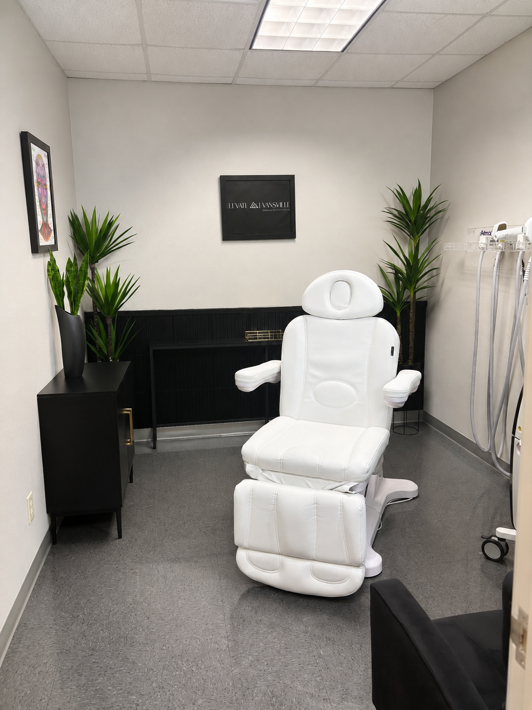Private treatment room at Elevate Evansville with a medical chair and the practice logo on the wall